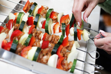 Shashlik cuisine. Metal sticks with vegetable and meat. Raw chicken, onion and bell pepper slices. Grilling food on a picnic. Girl in kitchen. Woman hands preparing dinner.