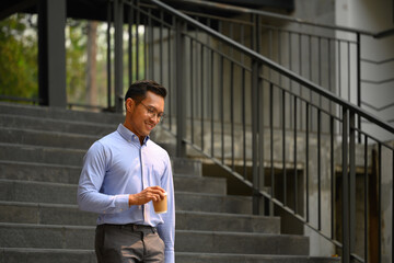 Smiling businessman holding take away coffee cup walking down the stairs outside a building