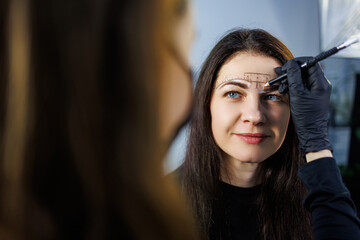 A permanent makeup artist marks a woman's eyebrows with a pencil. Cometological procedure of...