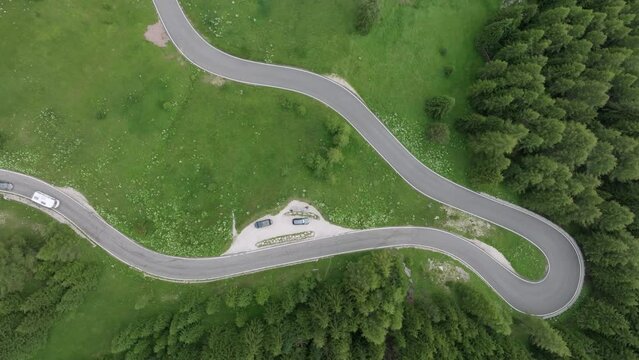 An aerial perspective captures multiple cars winding through the forested roads near Selva Pass in the Dolomite Mountains, Trentino, South Tyrol, Italy. LuPa Creative.