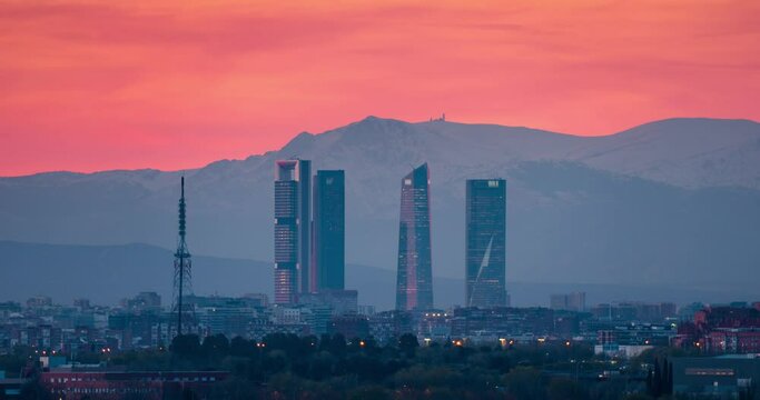 Timelapse of Madrid skyline with 5 towers business area CTBA and snowy Sierra mountain peaks as background sunset day to night time-lapse