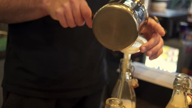 Side view of bartender pouring lemon juice in a bottle through a plastic funnel. Focus pull 4k shot