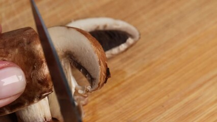 Female hand slicing royal champignon mushrooms on a cutting board with a knife.