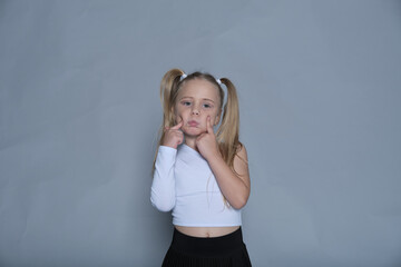 Child making a funny face, her pigtails adding to the silly, adorable gesture, standing against a...
