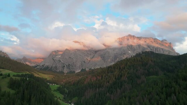 An evening aerial orbit view of the Sas dles Nü (Cima Nove) mountain covered in beautiful clouds. The drone is flying to the left above the valley in La Val village. South Tyrol, Italy. LuPa Creative.