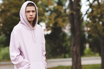 Serious sad teenage boy 16-18 year old wearing hood and pink hoodie outdoor close up. Looking at...