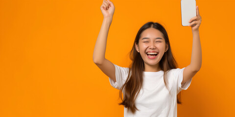 full length Happy Asian woman holding a smartphone and winning the prize on orange color background,High resolution professional photography - obrazy, fototapety, plakaty