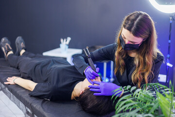 Permanent make-up of eyebrows. Woman professional permanent artist with a tool. A young permanent...