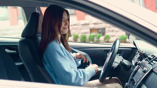 Young happy woman driver sitting inside car on city parking fastens seatbelt before driving for safe trip. Safety on road concept. Transport seatbelts importancy for accidents protection