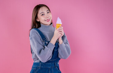 Portrait of happy korean model girl. Joyful adorable teenage girl smile broadly with eat tasty ice cream. Asian beauty woman has fun enjoys summer in stylish bib jeans clothes isolated on pink wall
