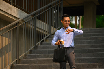 Attractive businessman in front of the building and checking time on wristwatch for appointment