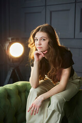A beautiful young girl is sitting on a sofa in the studio in the spotlight. Stylish loft interior. - 789174601