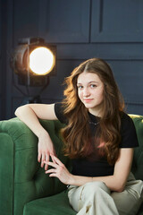 A beautiful young girl is sitting on a sofa in the studio in the spotlight. Stylish loft interior. - 789174609