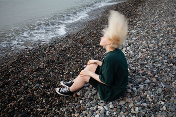 Portrait of young girl with short blonde bob hair and green dress on cold sea beach