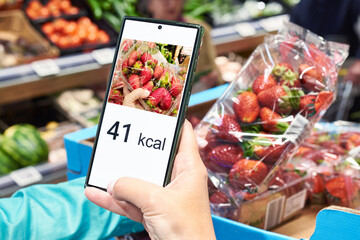 Checking calories on strawberry in store with smartphone