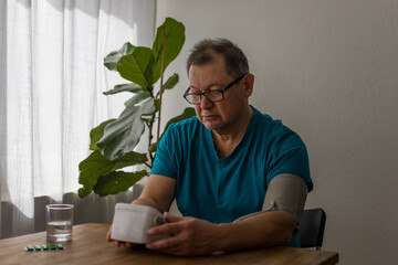 Seniory man checks blood pressure with monitor on upper arm in room smiling elderly gentleman measures blood pressure at home monitoring his health,
