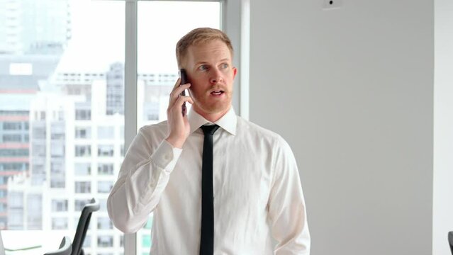 Busy young business man, 30 years old professional male executive manager talking on phone making business call on cellphone at work communicating by telephone walking in office.