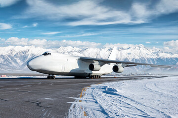 White wide body transport cargo airplane at winter airport on the background of high scenic mountains