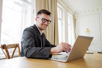 A content manager man with stylish glasses works intently on a laptop at a spacious table in a room...