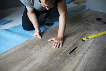 Installing laminated floor, detail on man hands blue wooden tile, over white foam base layer, small...