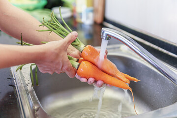 Woman hands washing fresh orange carrots in a kitchen - 789201016