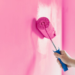 Close-up on the hand of a man who is painting a wall pink with a paint roller. Painting apartment,...