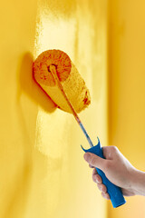 Close-up on the hand of a man who is painting a wall sunflower with a paint roller.  Painting apartment, renovating with sunflower color paint.