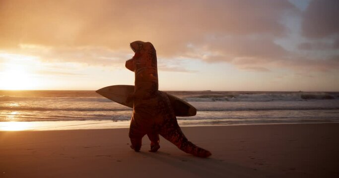 Surfboard, sunset and dinosaur costume on beach for water sports competition training for comedy. Goofy, running and inflatable t rex mascot by ocean or sea for surfing with comic or funny joke.