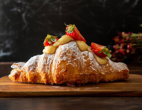 Freshly baked croissant, with strawberries and cream on top. Dark wooden background