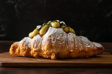 Freshly baked croissant, with pistachio cream and nuts on top. Dark wooden background