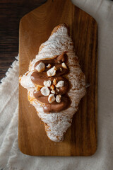 Freshly baked croissant, with chocolate and nuts on top. Dark wooden background.