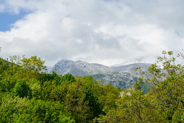 Outdoors, snow-capped mountains in April with green trees - 789212047