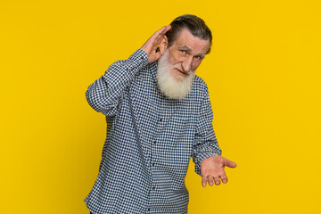 I can't hear you. What. Senior old man trying hear you looking confused frowning keeping arm near ear for louder voice asking to repeat to hear information deafness. Grandfather on yellow background