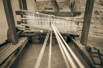 An old wooden loom with several threads stretched to it. Focus on the middle of the machine. Sepia