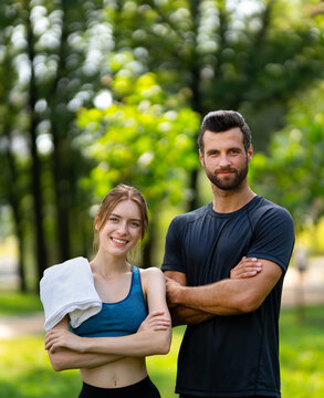 Portrait image of young couple  outdoors fitness sport training exercising. Woman man, male bearded coach trainer, stand with crossed arms in public park. Sport, cross fit, healthy lifestyle concept.