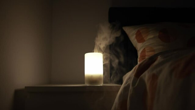 Static shot of an essential oil diffuser on a nightstand emitting a warm light
