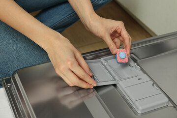 Woman putting detergent tablet into open dishwasher, closeup