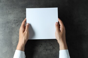 Man holding blank book at black textured table, top view. Mockup for design