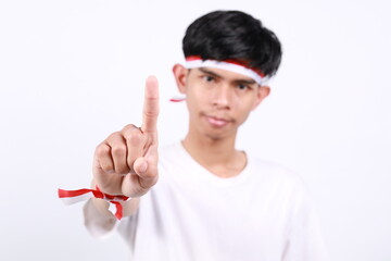 Naklejka premium Asian young boy with red white ribbon for celebrating Indonesia independence day standing while showing a finger. Selective focus on hand