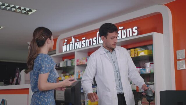 A male pharmacist scans medication at a fully stocked pharmacy counter, The neon sign in Thai reads "Pharmacist Service Area"