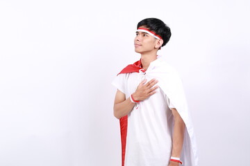 Asian young boy with red white ribbon for celebrating Indonesia independence day standing with salute hand gesture while looking side above