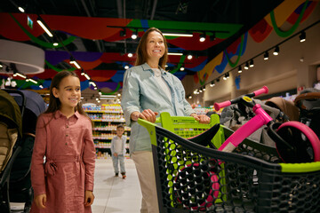 Positive pregnant mother and daughter doing purchases at toys store department - obrazy, fototapety, plakaty