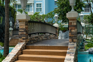 A stone bridge with decorative lanterns and steps spans a blue water pool in a condominium in a...