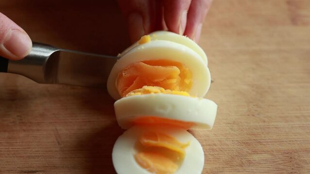 A close-up stock video capturing the hands of a woman delicately slicing a boiled egg on a wooden cutting board, showcasing the simplicity and precision of meal preparation.
