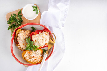 Stuffed bell peppers on white kitchen table background. Colorful red, yellow, green peppers with diet chicken minced meat, vegetables and rice, with white sauce, Balanced healthy food recipe