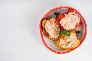 Stuffed bell peppers on white kitchen table background. Colorful red, yellow, green peppers with diet chicken minced meat, vegetables and rice, with white sauce, Balanced healthy food recipe