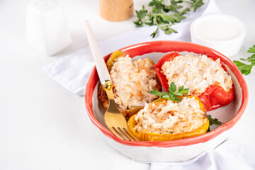 Stuffed bell peppers on white kitchen table background. Colorful red, yellow, green peppers with diet chicken minced meat, vegetables and rice, with white sauce, Balanced healthy food recipe