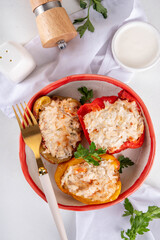 Stuffed bell peppers on white kitchen table background. Colorful red, yellow, green peppers with diet chicken minced meat, vegetables and rice, with white sauce, Balanced healthy food recipe