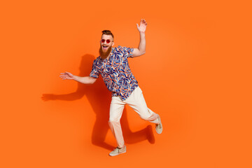 Full length photo of eccentric guy with red beard in sunglass wear print shirt dancing having fun isolated on orange color background
