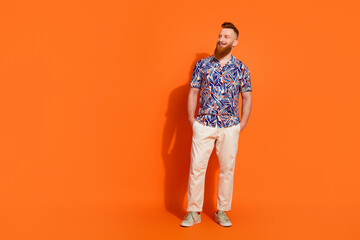 Full length photo of extravagant guy wear print shirt look at discount empty space arms in pockets isolated on orange color background